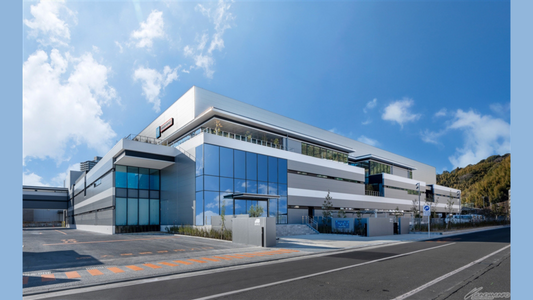 New Bandai Hobby Center factory exterior in Shizuoka with mirrored glass façade and BHCPDII signage under a clear sky.