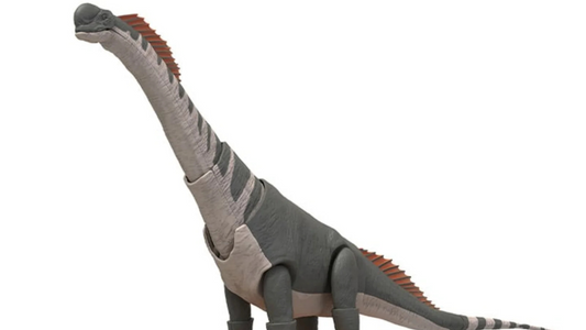 Assembled Titanosaurus plastic model with grey and tan body, long neck and tail, orange back plates, standing on a textured base in Plannosaurus series.