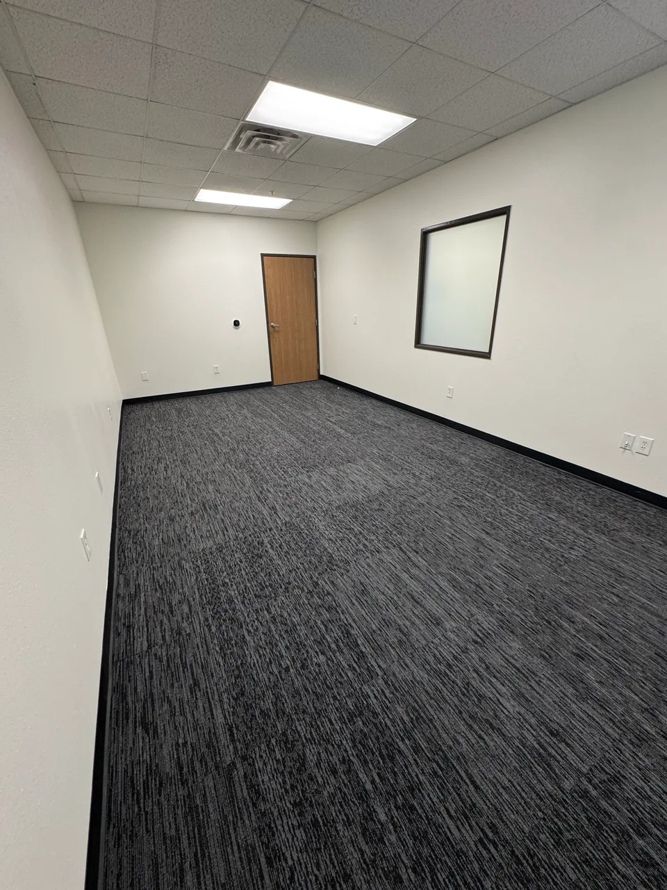 Another angle of the empty Artrovo Gundam space, showing a wooden door, interior window and gray carpet.